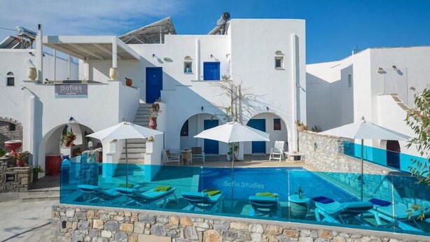 A white building with a pool area, blue doors, and outdoor seating. - Studios Sofia (Naxos)