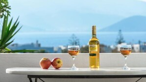A table with two glasses of wine, a bottle of wine, and two apples on a balcony with a view of the sea and mountains. - Studios Sofia (Naxos)