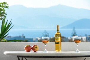 Una mesa con dos copas de vino, una botella de vino y dos manzanas en un balcón con vistas al mar y a las montañas.