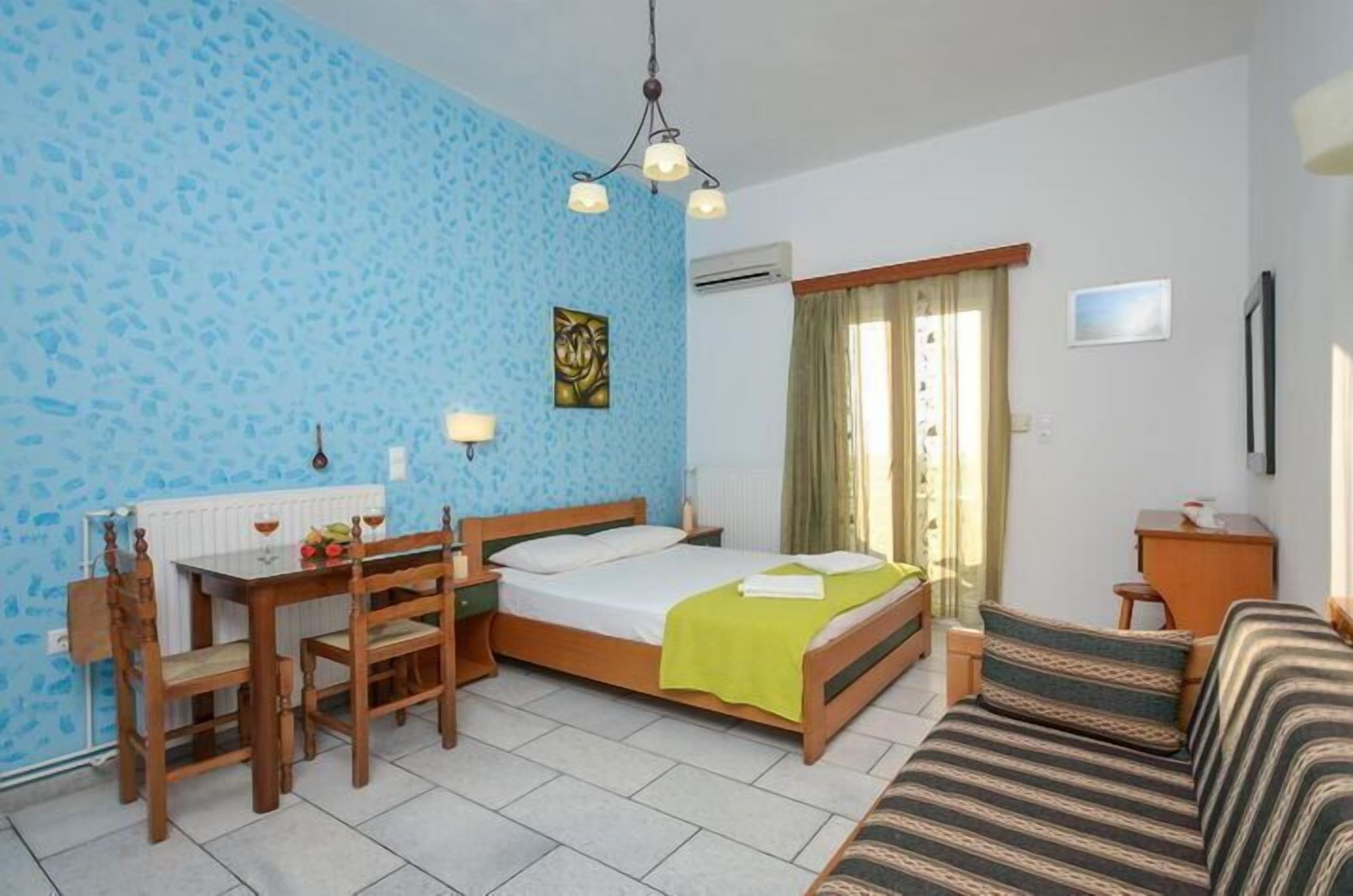 Um quarto com cama, escrivaninha com cadeiras, sofá, janela com cortinas e um quadro na parede.