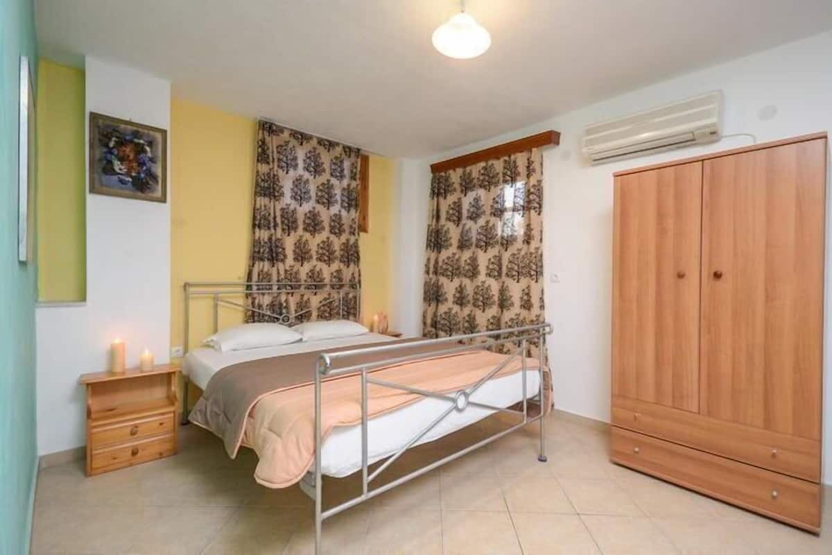 Quarto com cama, mesa de cabeceira, cortinas, guarda-roupa e ar condicionado.