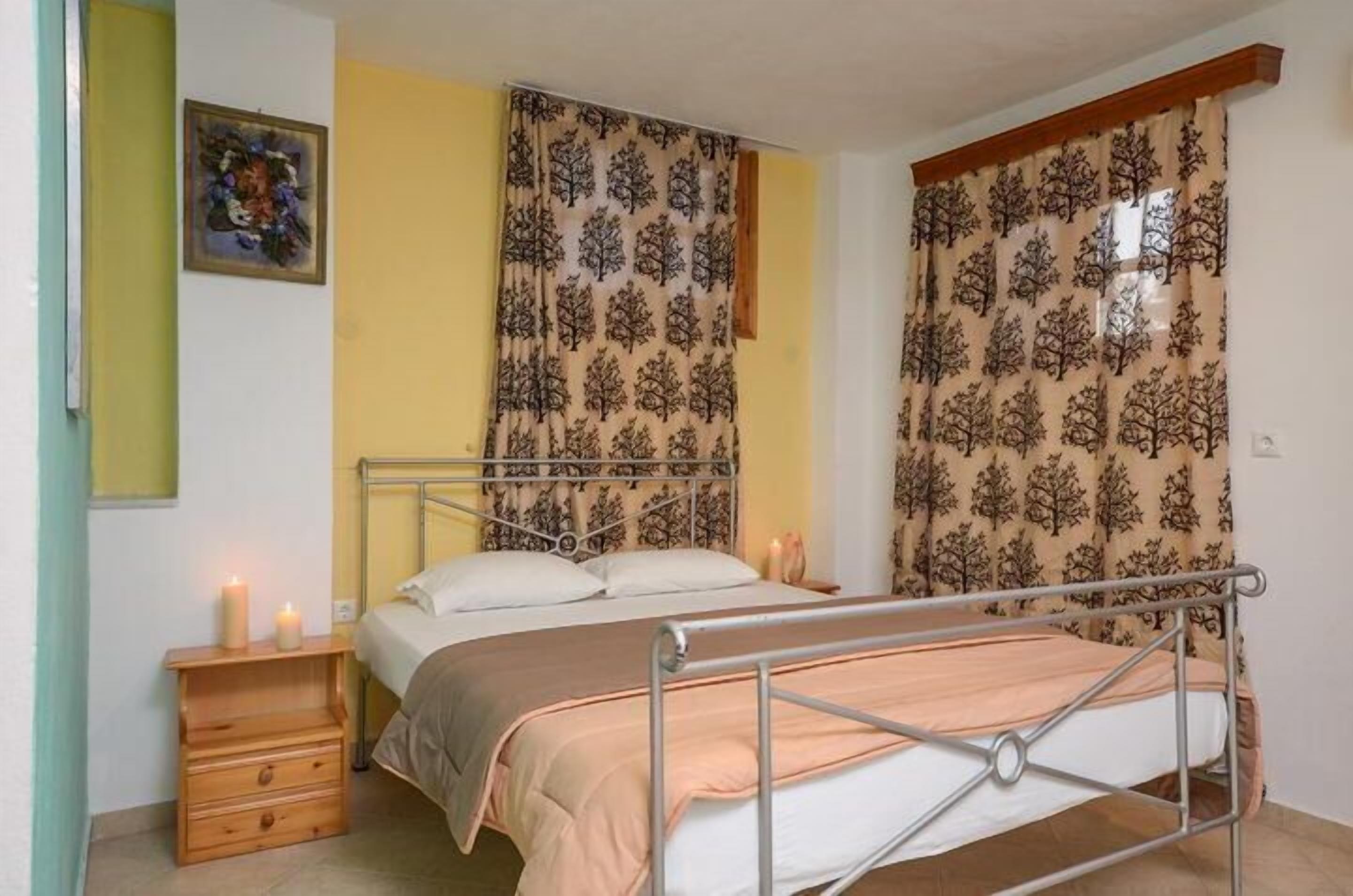 Un dormitorio con estructura de cama metálica, una mesita de noche de madera con cajones y una sola mesita auxiliar.