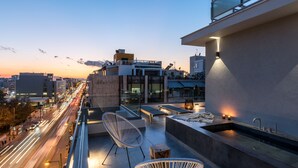 A rooftop terrace with modern seating, a built-in sink, and a city view at dusk.
