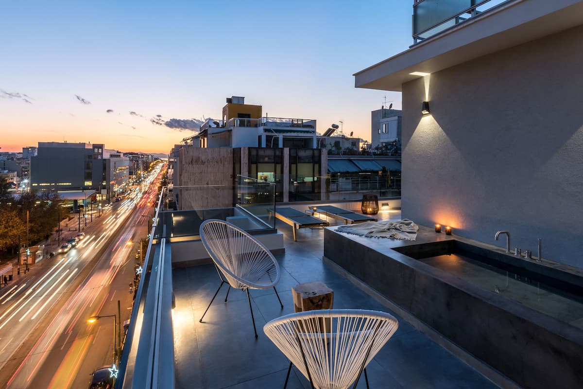 A rooftop terrace with modern seating, a built-in sink, and a city view at dusk.