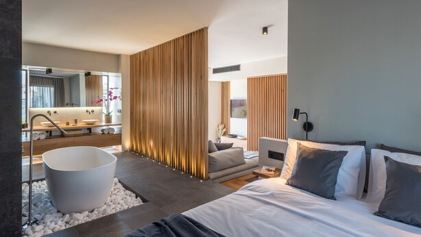 A modern hotel room with a large bed, a bathtub, a sofa, and a desk.