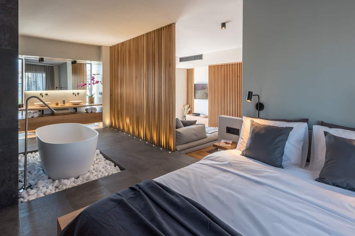 A modern hotel room with a large bed, a bathtub, a sofa, and a desk.