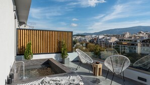 A rooftop terrace with a pool, two white wire chairs, a striped blanket, and a wooden slatted wall.