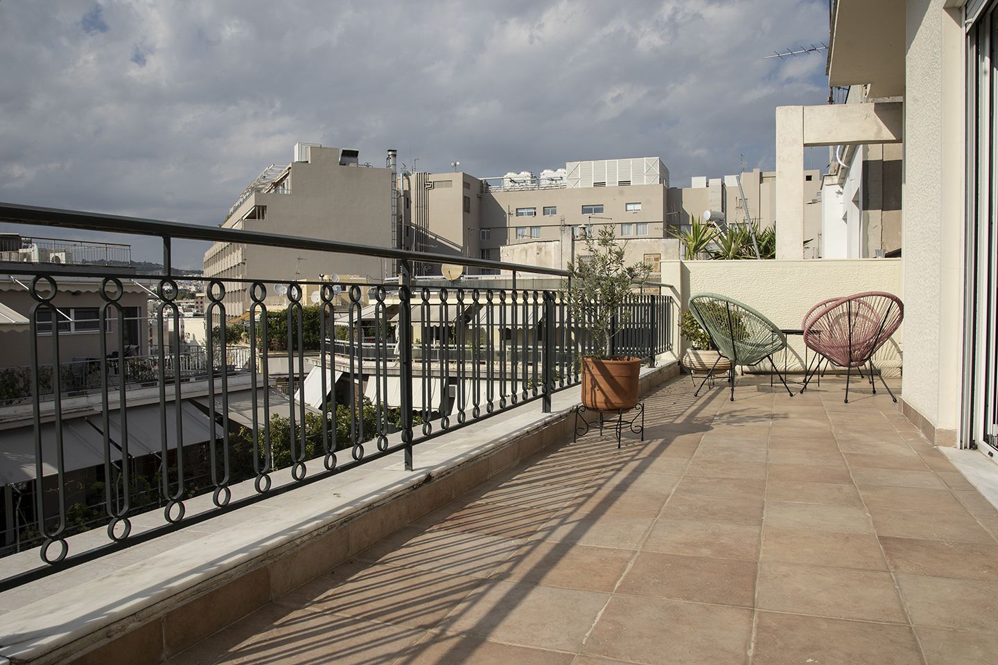 A rooftop terrace with a metal railing, a potted plant, and two wicker chairs.