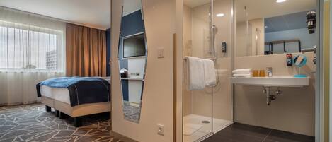 A hotel room with a bed, a shower, a sink, and a mirror.