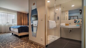 A hotel room with a bed, a shower, a sink, and a mirror.