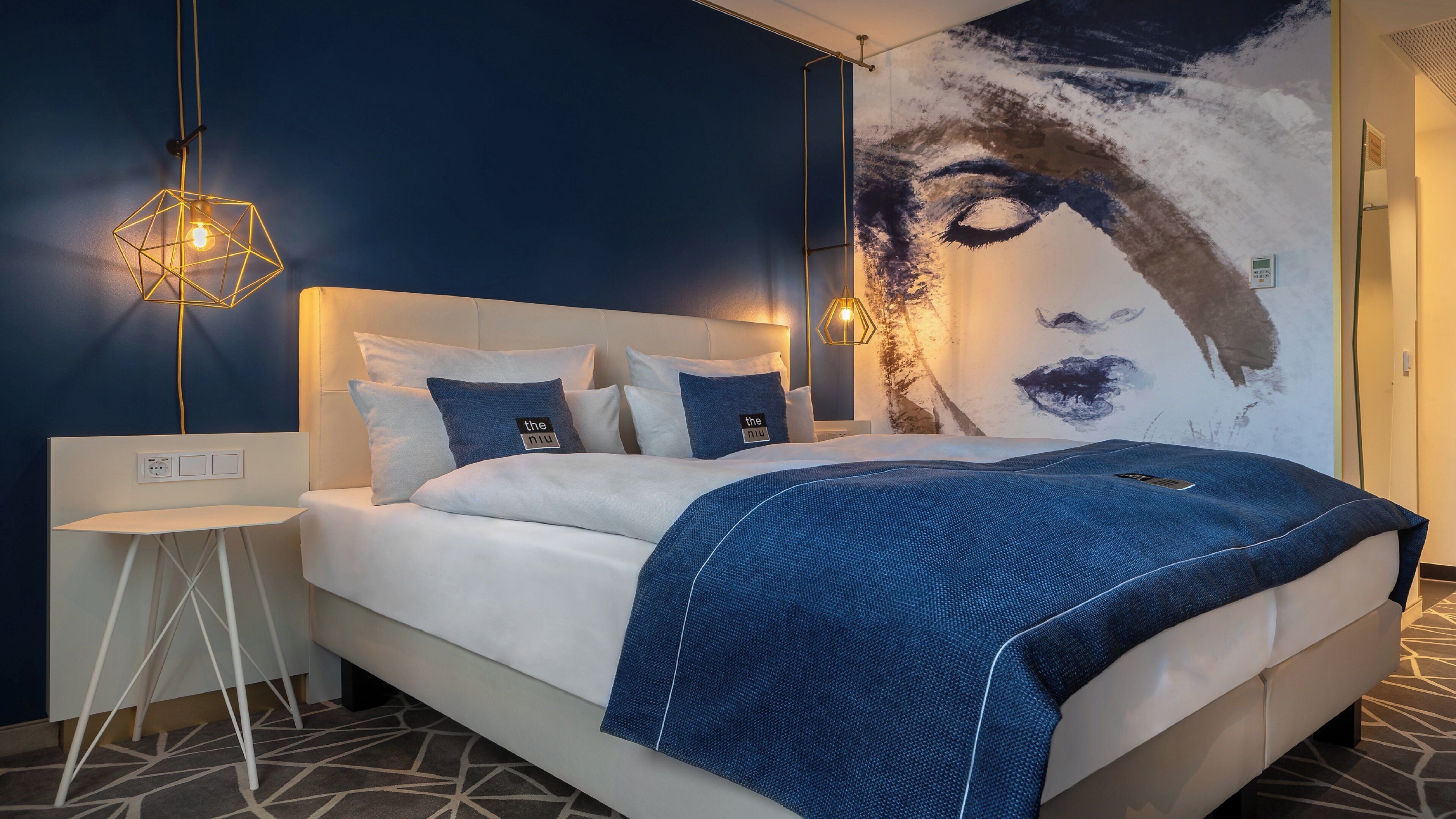 Un dormitorio moderno con una cama grande, varios almohadones, una mesita de noche y una obra de arte colgada en la pared.