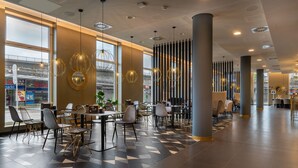 A modern restaurant with a geometric floor pattern, contemporary furniture, and large windows offering views of the street. - Holiday Inn - the niu, Ridge Halle Central Station by IHG (Halle (Saale))