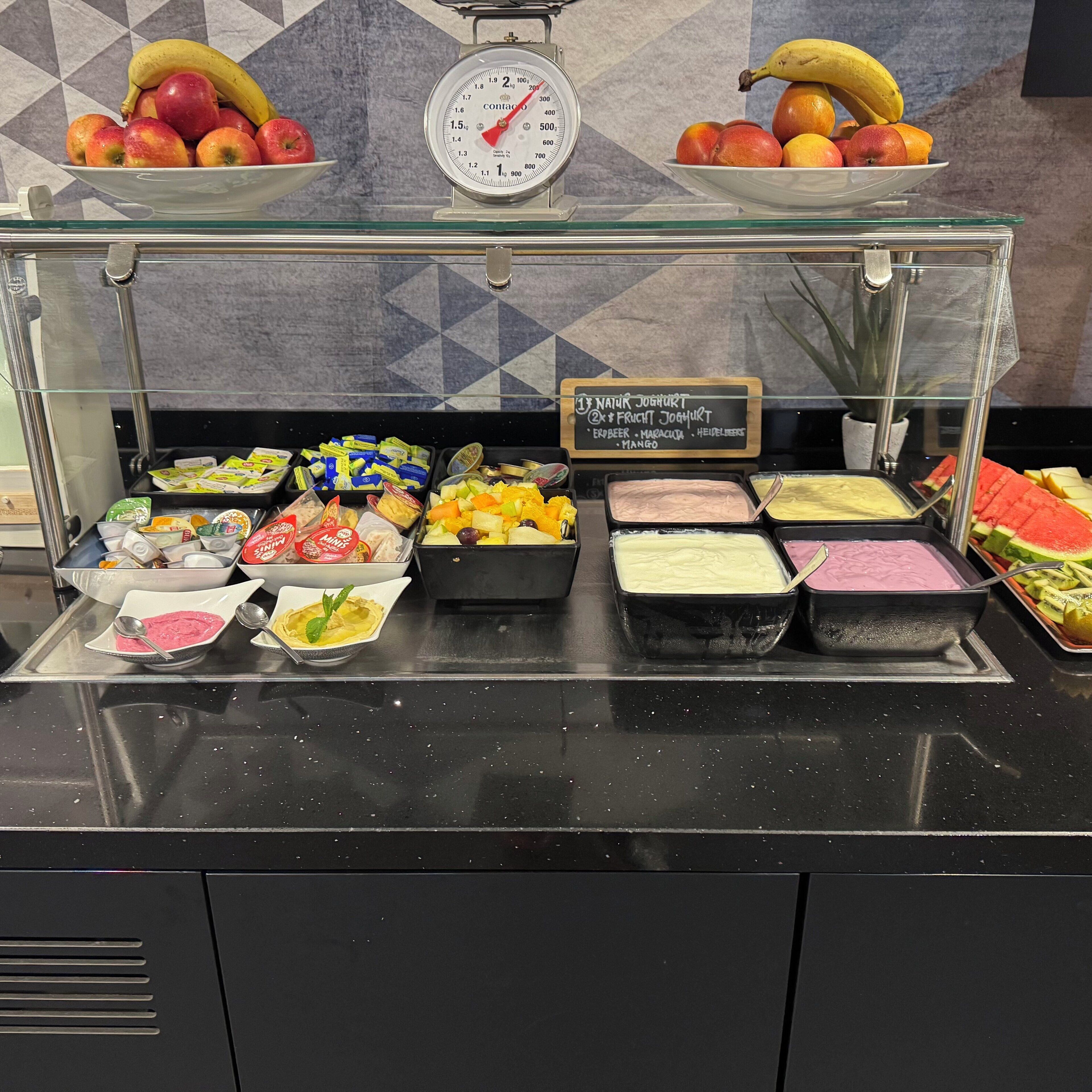 A buffet with various food items including fruits, yogurts, and desserts.