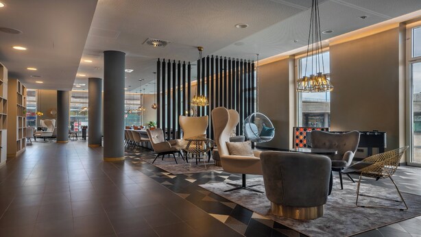 A spacious lobby with modern furniture, a large seating area, and a view of the city through large windows. - Holiday Inn - the niu, Ridge Halle Central Station by IHG (Halle (Saale))