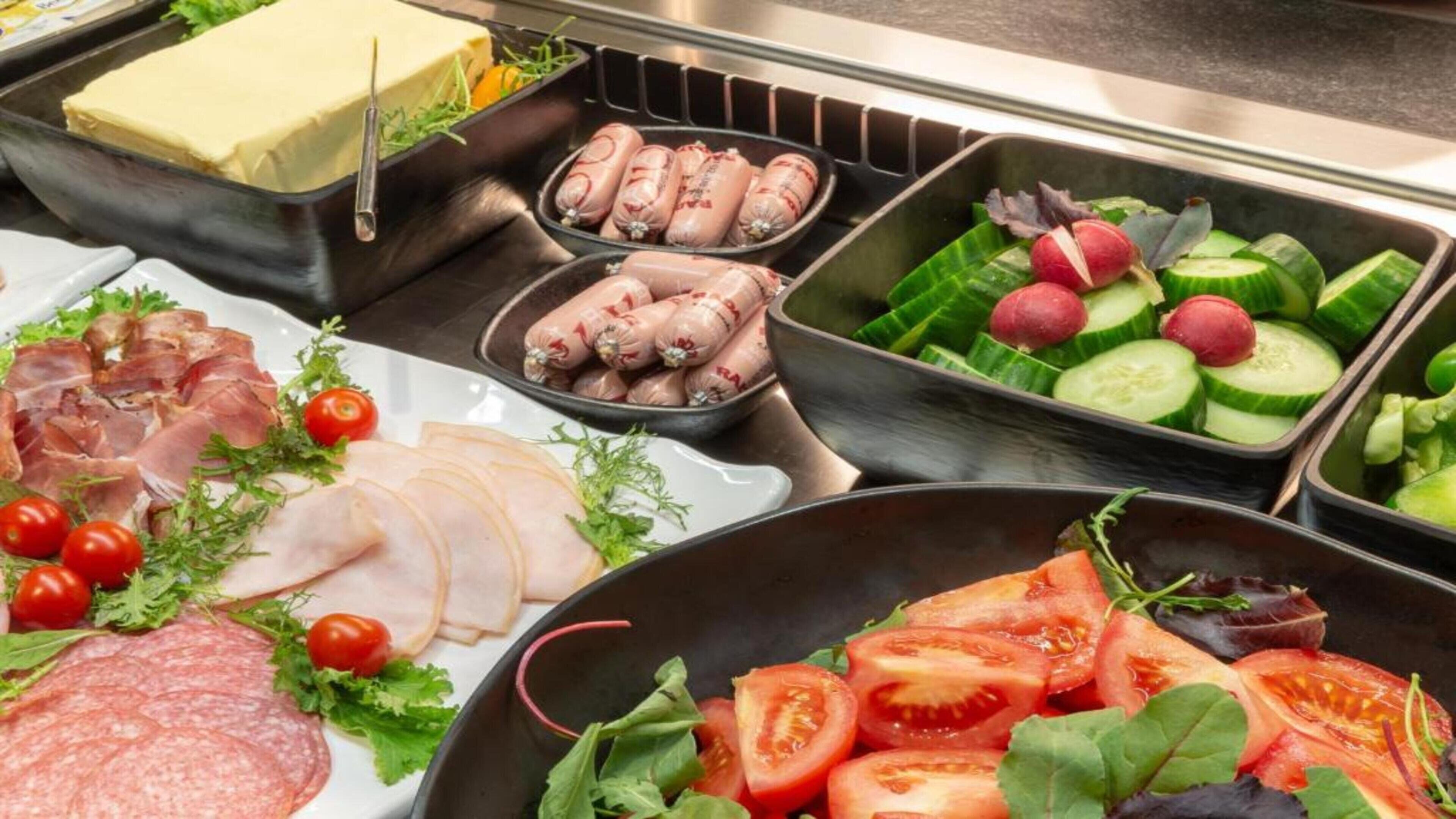 A buffet with various food options including sliced meats, cheeses, and fresh vegetables.
