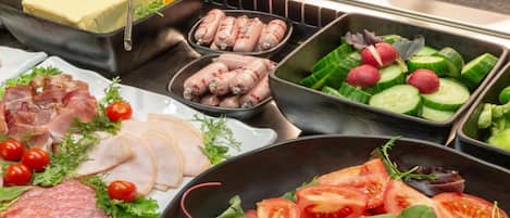 A buffet with various food options including sliced meats, cheeses, and fresh vegetables.