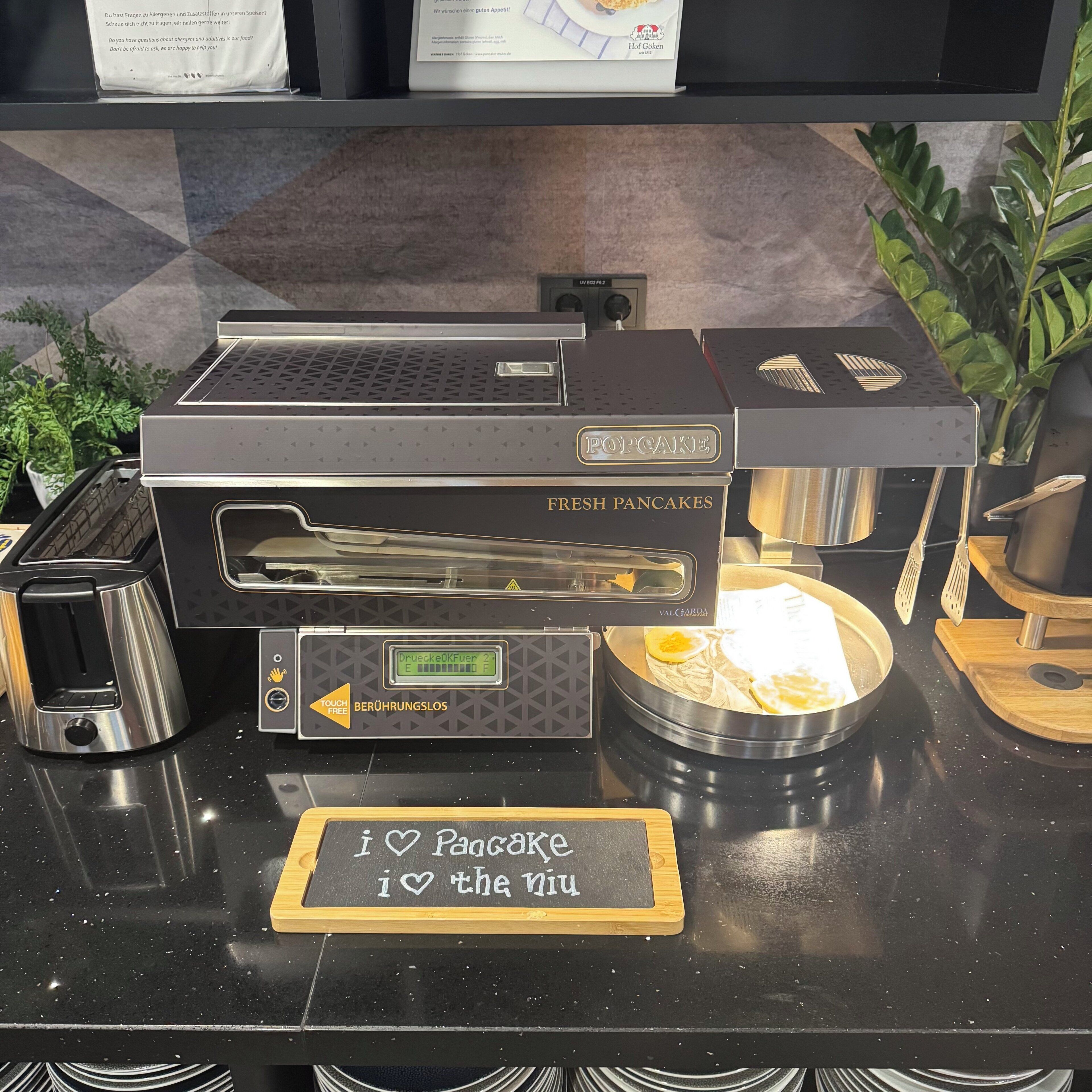 A kitchen counter with a toaster, a pop-up toaster, a digital display, and a sign that says 'I love Pancake.'
