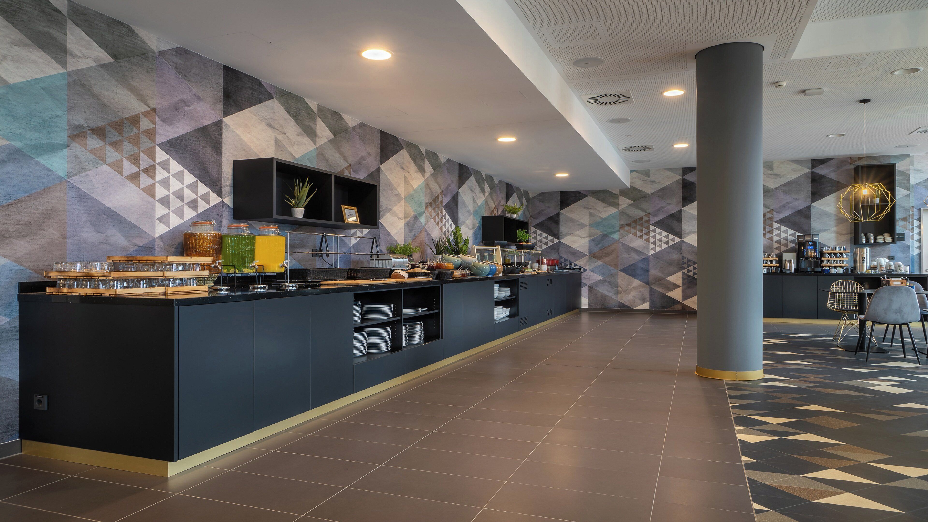 Eine moderne Hotelhalle mit einer langen Rezeption, einer Kaffeestation und einer Sitzecke mit Stühlen und einem Tisch.