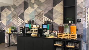 A modern kitchen area with a geometric patterned wall, a black counter with coffee machines, and a sign indicating the kitchen.