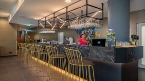 A modern bar area with a marble countertop, gold wire chairs, and a bartender. - Holiday Inn - the niu, Ridge Halle Central Station by IHG (Halle (Saale))
