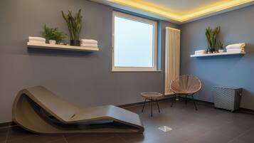 A modern spa room with a reclining chair, two small tables, and potted plants on floating shelves.