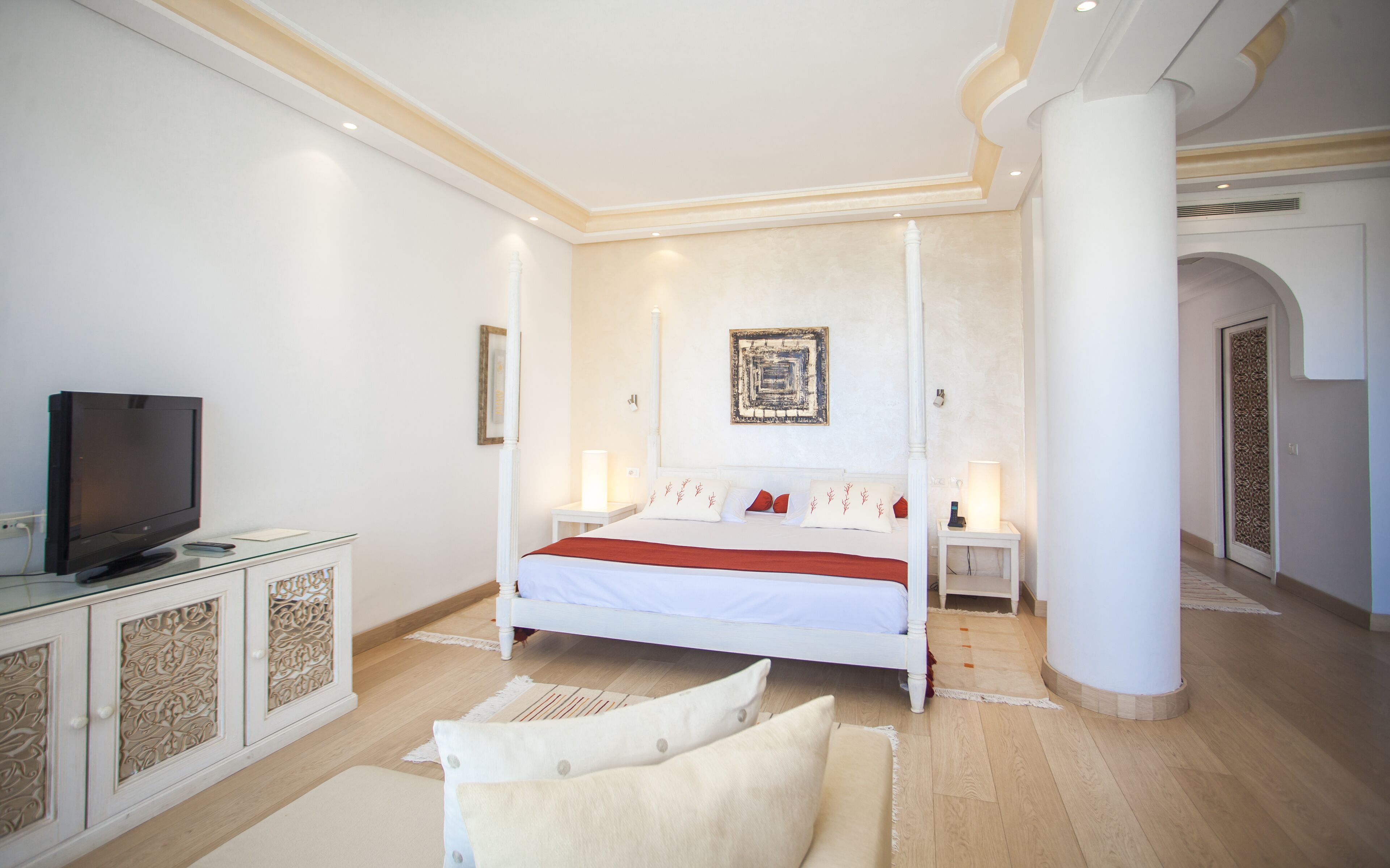 A modern bedroom with a large bed, a television on a cabinet, and a decorative wall piece.