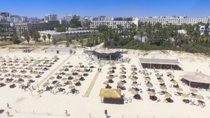 Una playa con numerosas tumbonas y sombrillas, una pequeña cabaña y un edificio de techo curvo.