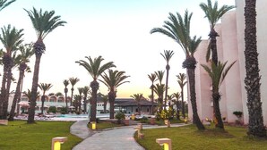 Un camino conduce a una zona de piscina rodeada de palmeras y un edificio de diseño moderno.