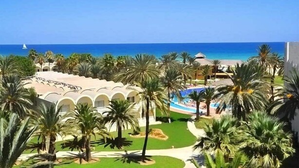 Un resort con piscina, palmeras y vistas al océano.