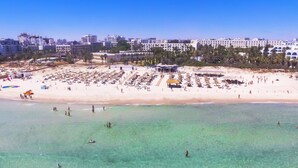 Una playa con muchos sombrillas y tumbonas, un cielo azul despejado y edificios al fondo.