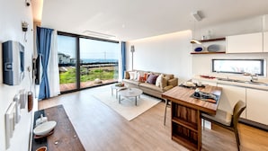 A modern living room with a sofa, coffee table, and dining table. There is a large window with a view of the outdoors. - The Aewol House (Jeju City)