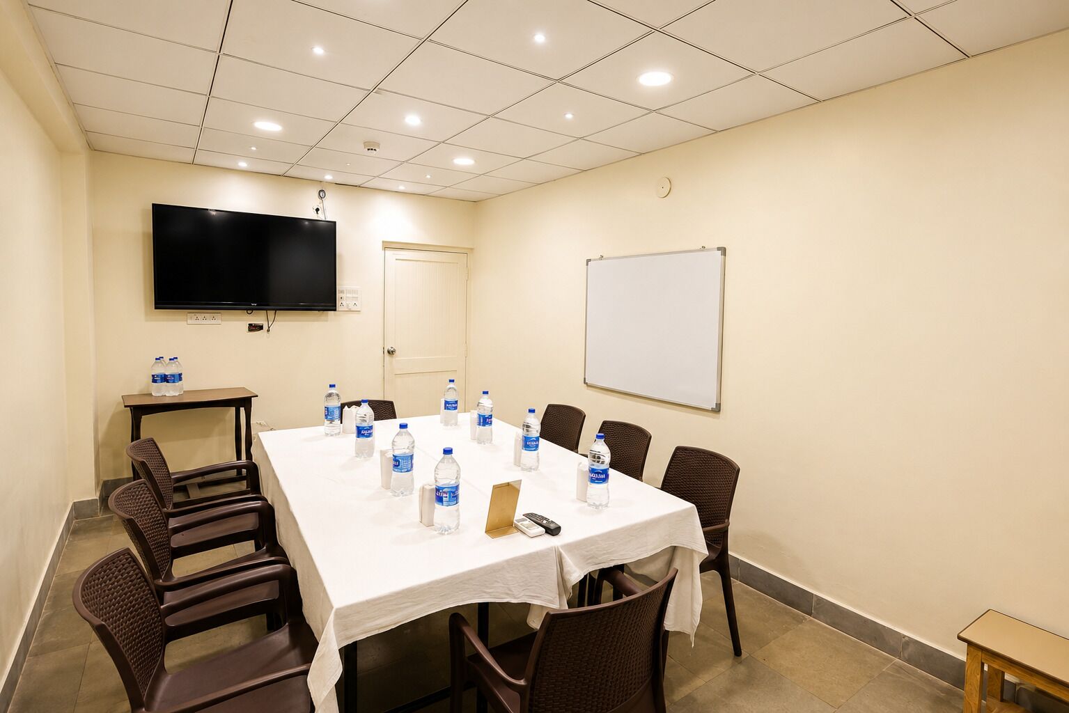 Una sala de conferencias con una larga mesa, sillas, una pizarra, un televisor de pantalla plana y botellas de agua.
