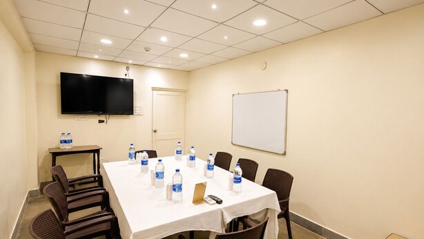 Una sala de conferencias con una larga mesa, sillas, una pizarra, un televisor de pantalla plana y botellas de agua.