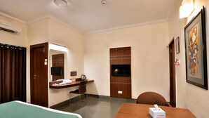 Una habitación de hotel con una cama, un escritorio con una silla, un televisor y una mesa con una caja de pañuelos.