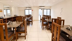 Un comedor limpio y bien iluminado con mesas y sillas de madera, piso de baldosas y un letrero de prohibido fumar en la pared.