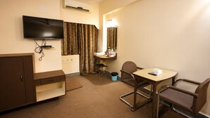 Habitación de hotel con televisión, escritorio y silla, espejo y un basurero.