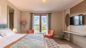 Habitación de hotel con una cama grande, televisión, zona de estar con sillas y vista a las montañas por la ventana.