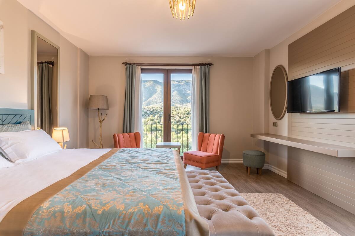 Habitación de hotel con una cama grande, televisión, zona de estar con sillas y vista a las montañas por la ventana.