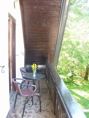 A balcony with a table and two chairs, a wooden ceiling, and a view of greenery. - Tourist house Capricorn (Bled)