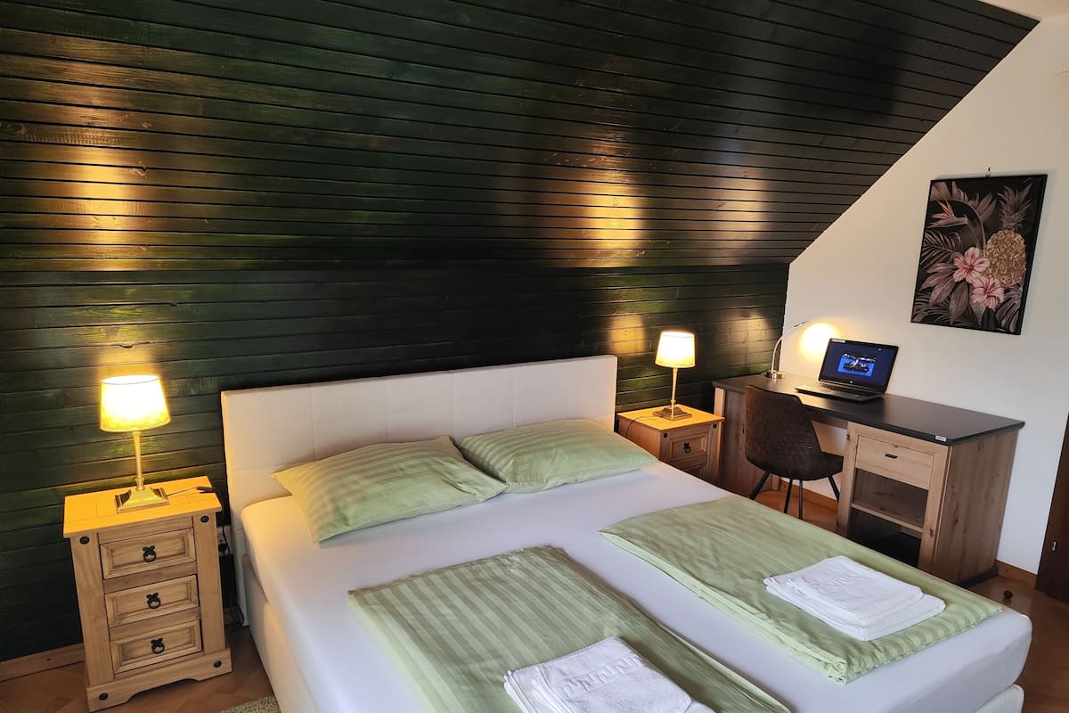 A bedroom with a bed, two bedside tables with lamps, a desk with a laptop, and a chair.