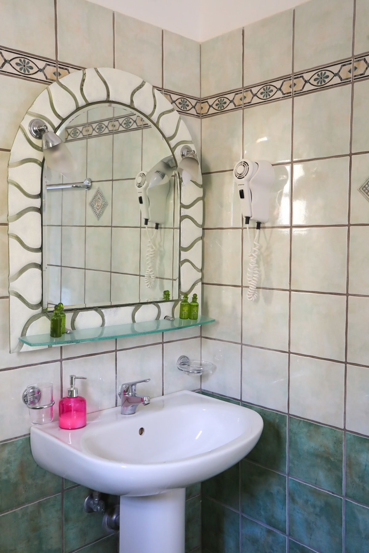 A bathroom with a white sink, a glass shelf with toiletries, and a mirror with a decorative frame.