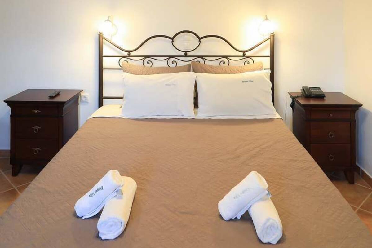 Un lit bien fait, avec deux serviettes enroulées, un lustre et des tables de chevet.