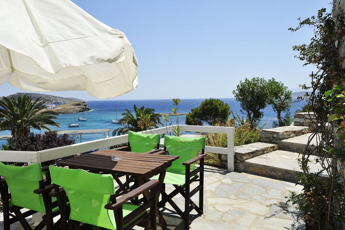 Une terrasse avec une table et des chaises, offrant une vue sur la côte, avec des bateaux et de la végétation.