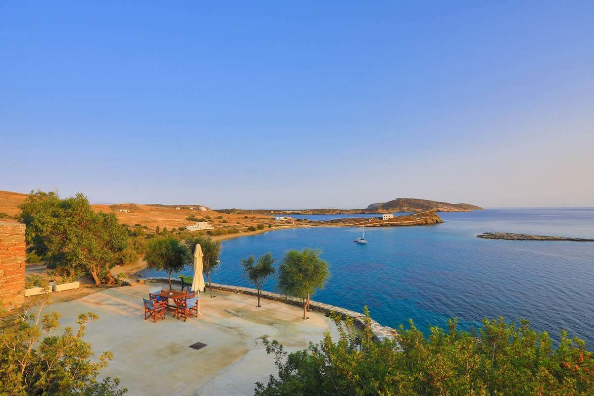 A coastal view with a patio area featuring outdoor furniture and a view of the sea and distant land.
