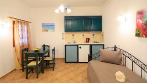Een compacte kamer met een bed, een kleine kitchenette, een eettafel met stoelen en een raam met gordijnen.
