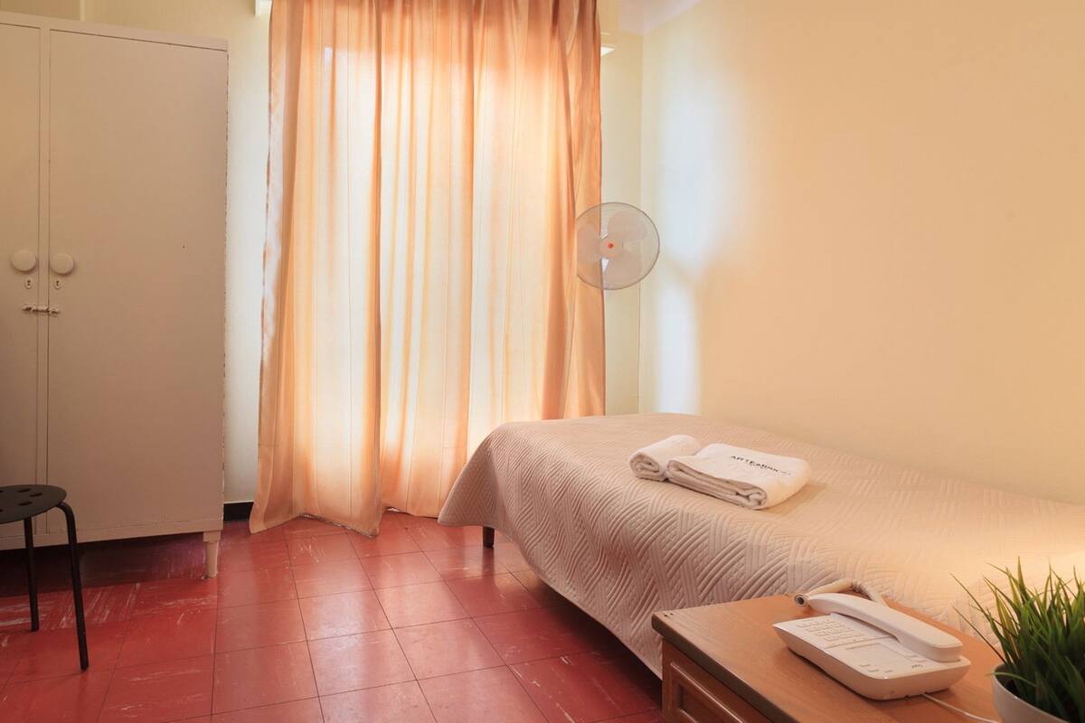 Une chambre d’hôtel comprenant un lit, un bureau avec une télévision, une chaise, une table de chevet avec un téléphone et une fenêtre avec des rideaux.