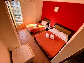 Habitación de hotel con dos camas, una mesita y una ventana con vista a edificios.