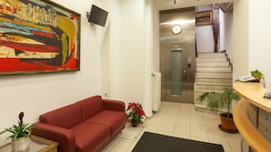 A reception area with a red sofa, a large abstract painting, a clock, and a staircase leading to an elevator. - Artemision (Athens)