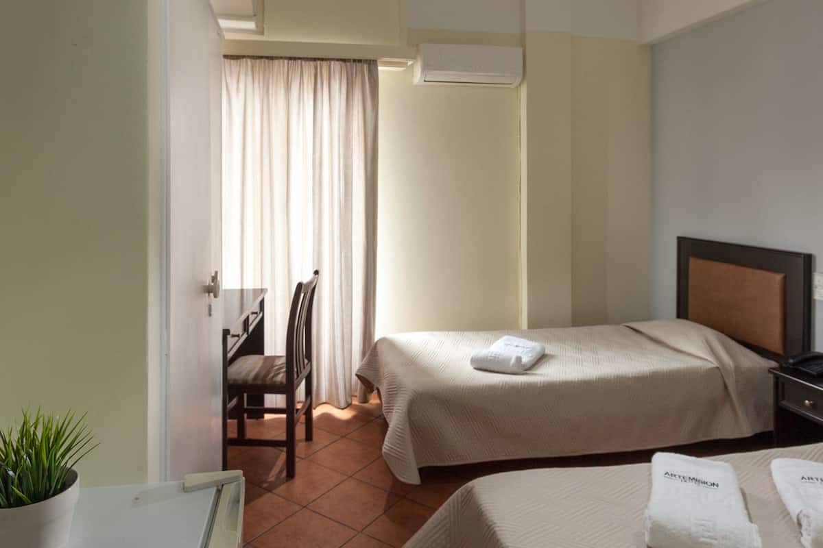 Une chambre d’hôtel avec deux lits, une chaise, un bureau et une plante en pot.