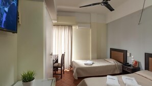 A hotel room with two beds, a TV, a ceiling fan, a potted plant, and a desk. - Artemision (Athens)